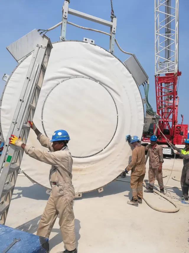 Workers positioning a large fabricated HDPE tank section during a crane lift in Kuwait