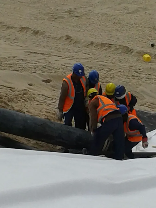 Crew laying large HDPE pipe over a geomembrane-lined slope on a Kuwait site