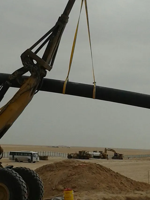 Crane lifting a long HDPE pipe string on a desert pipeline route in Kuwait
