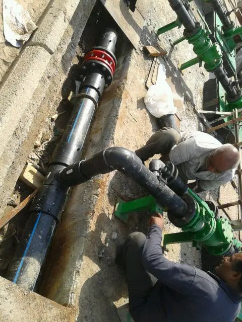 Workers connecting HDPE pipe with a flange adaptor and gate valve in a trench in Kuwait