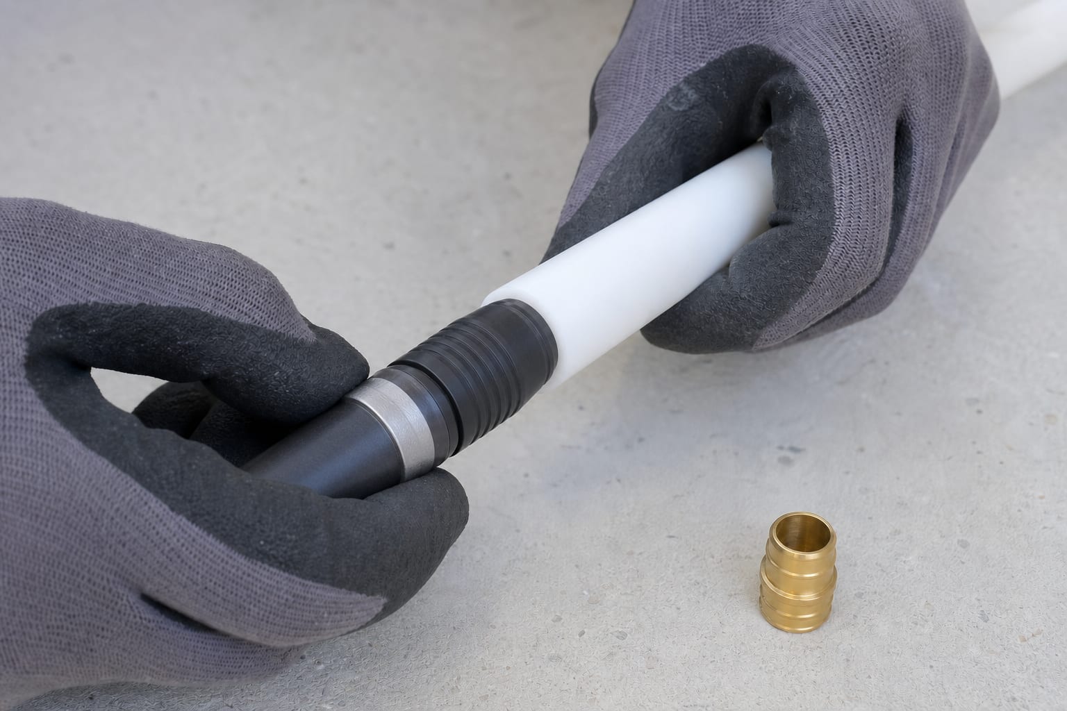 Gloved hands working a cold-expansion tool into the end of a white PE-Xa pipe, with a brass insert fitting waiting alongside and no flame in use