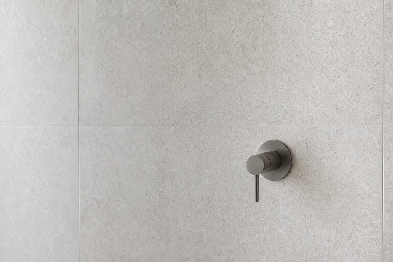 Finished residential bathroom wall in pale stone tile with a single brushed-steel mixer tap